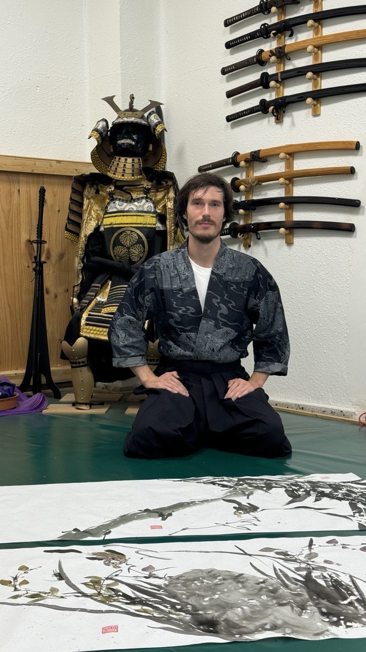 Mansur Kohaku kneeling in the dojo before his sumi-e calligraphy, beside the samurai armour